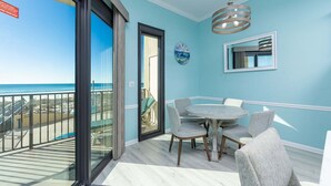 A balcony with a view of the beach, a round table with chairs, and a clock on the wall.