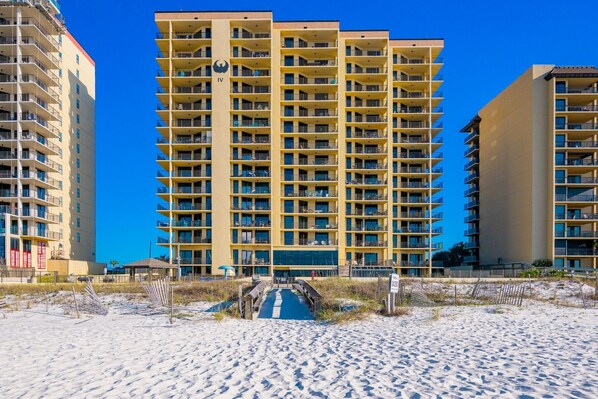 Un hotel de gran altura con varios balcones, una entrada central y una playa de arena.