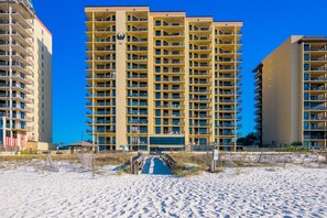 A high-rise hotel with multiple balconies, a central entrance, and a sandy beach area in front. - Phoenix Iv 4005 3 Bedroom Condo (Orange Beach)
