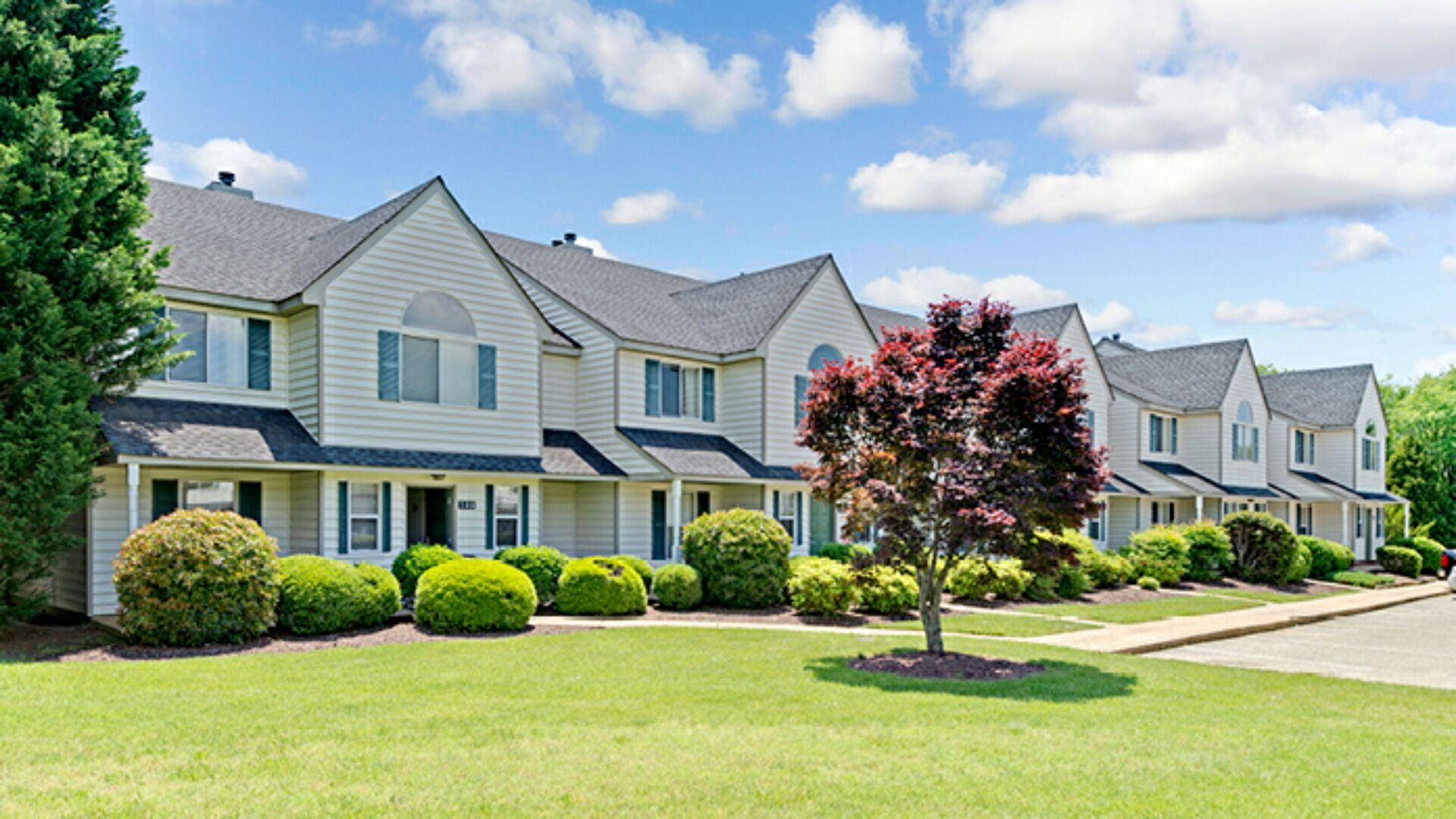 A row of two-story houses with a well-maintained lawn and trimmed bushes.