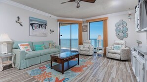 A living room with a sofa, armchairs, a coffee table, and a view of the ocean through large windows.