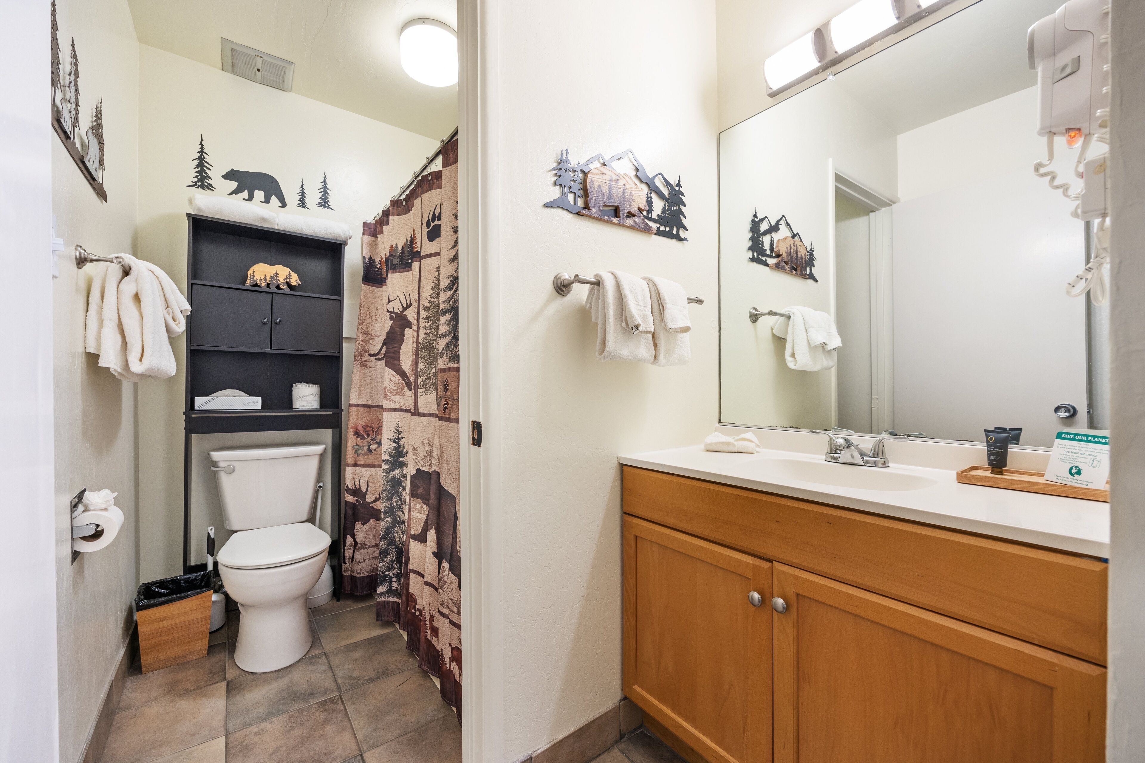 A bathroom with a toilet, a sink, and a mirror. There are towels hanging on the wall and a cabinet with a bear decoration.