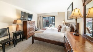 A hotel room with a bed, a dresser, a TV, a desk, and a window with a view of a building and trees. - 222 Bldg B 1 Bedroom Condo (Truckee)