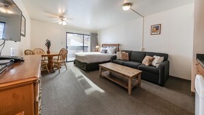 Habitación de hotel con cama, sofá, mesa de centro, televisor y escritorio con computadora.