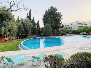 Une piscine à bordures courbes, entourée d’une terrasse dallée et de chaises longues vertes.