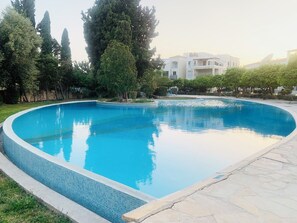 Una piscina con borde de azulejos, rodeada por un solárium de piedra y vegetación.