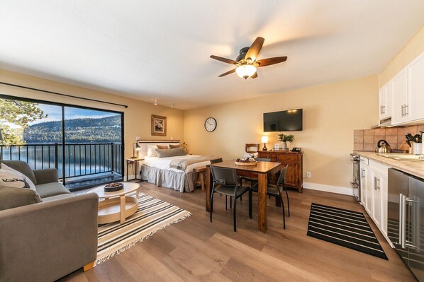 A modern hotel room with a balcony, a dining area, and a kitchen.