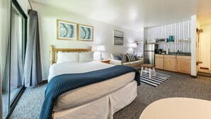 Habitación de hotel con cama, sofá, una mesita, zona de cocina y ventana con cortinas.