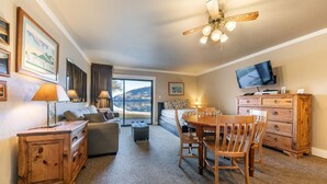 A cozy hotel room with a large window offering a scenic view, a wooden dining table, a comfortable sofa, and a television. - 146 Bldg C 1 Bedroom Condo (Truckee)