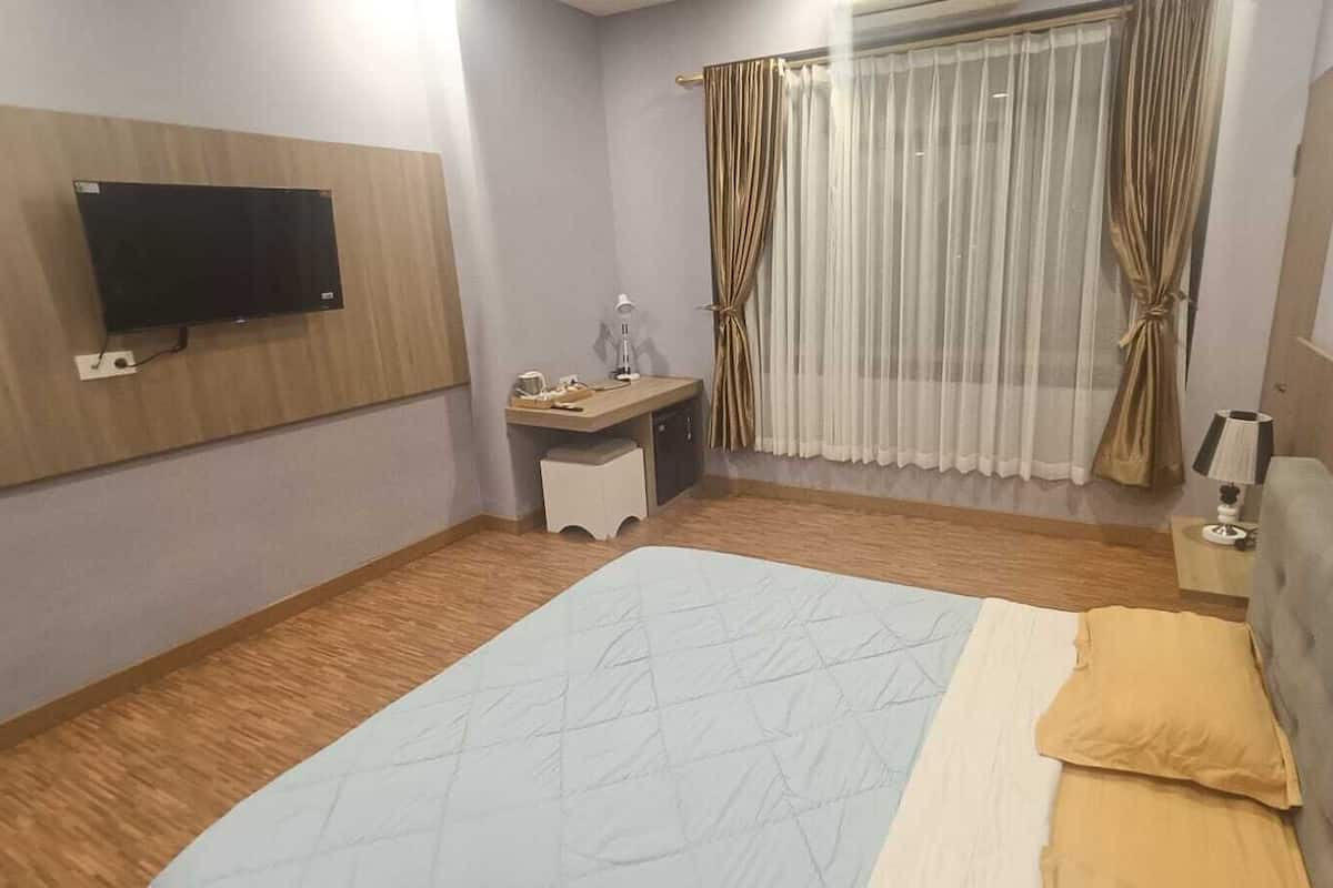 Ein Hotelzimmer mit Bett, Schreibtisch, Sessel, Wandfernseher und einem Vorhangfenster.