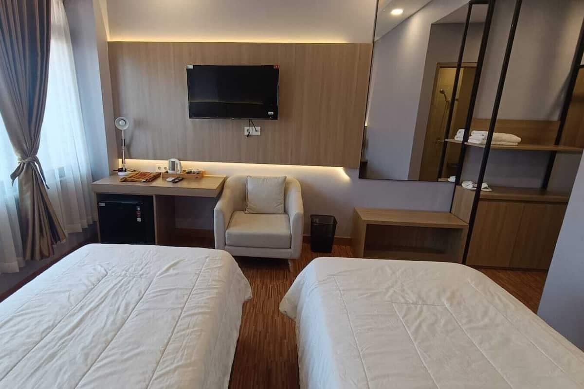 Ein Hotelzimmer mit zwei Betten, einem Schreibtisch, einem Stuhl, einem Fernseher und einem Spiegel.