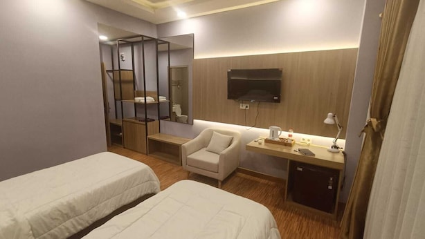 Ein Hotelzimmer mit zwei Betten, einem Schreibtisch mit Fernseher, einem Sessel und einem kleinen Tisch mit Lampe.