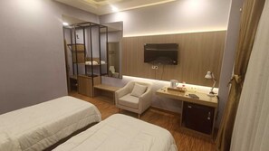 Une chambre d’hôtel avec deux lits, un bureau avec une télévision, une chaise et une petite table avec une lampe.