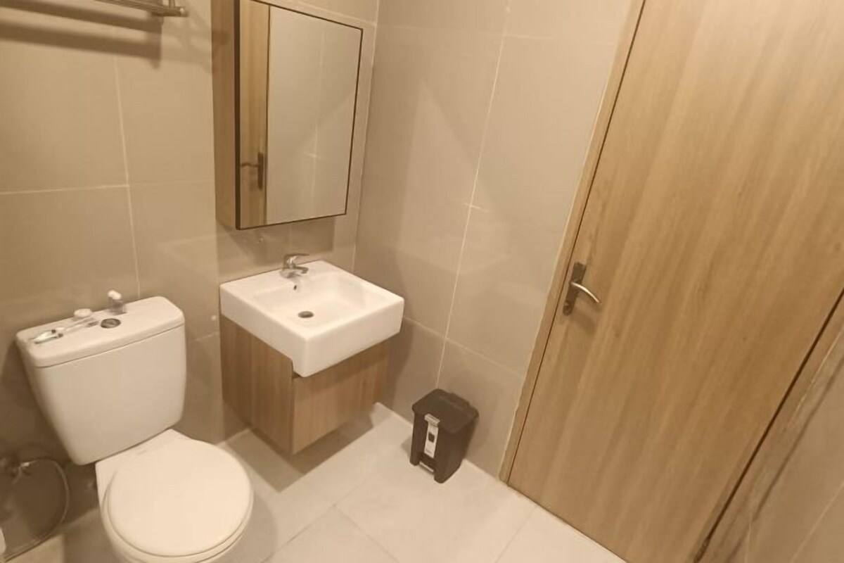 Baño con inodoro, lavamanos, espejo y puerta de madera.