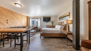 Quarto de hotel com teto de madeira, uma cama, escrivaninha, cadeira, televisão e janela.