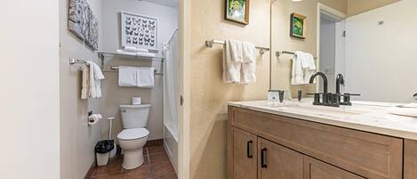 A bathroom with a toilet, sink, and cabinet. There are towels hanging on the wall and a trash can.