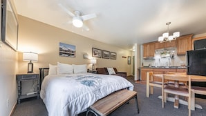 Une chambre d’hôtel équipée d’un lit, d’un bureau, d’une chaise, d’un banc, d’une kitchenette et d’un ventilateur de plafond.