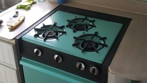 Una cocina con estufa color aguamarina, armarios blancos y ventana con vistas.
