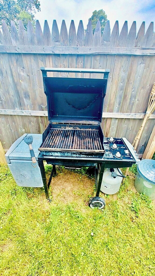Un barbecue avec un couvercle noir, un brûleur à gaz et un brûleur latéral, installé sur une pelouse verdoyante, avec une clôture en bois en arrière-plan.