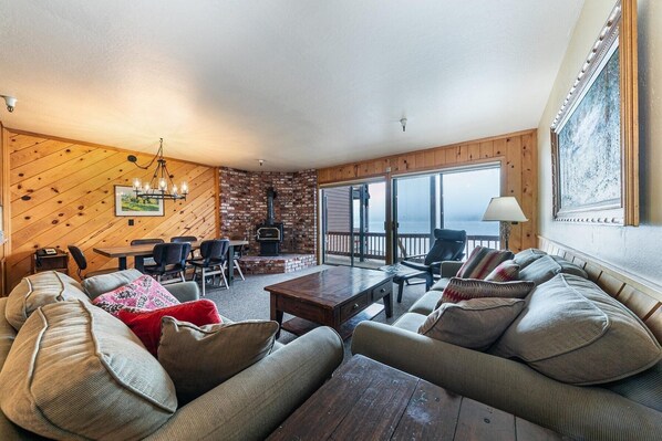 Een gezellige woonkamer met een open haard, houten wanden en een groot raam met uitzicht op een balkon.