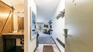 Un couloir étroit, avec un banc en bois sur la gauche, un paillasson au centre et une porte avec une poignée sur la droite.