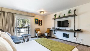 Une chambre d’hôtel avec un lit, une télévision, un bureau et une chaise. Elle dispose d’un balcon avec vue sur l’extérieur.