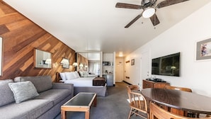 A hotel room with a wooden herringbone wall, a sofa, a bed, a desk with a chair, a ceiling fan, and a TV. - 135 Bldg C 1 Bedroom Condo (Truckee)