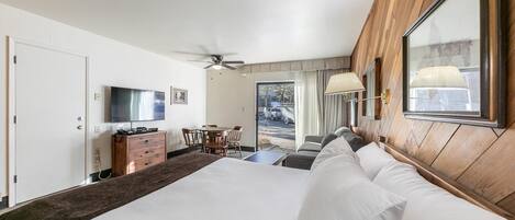 A hotel room with a large bed, a desk with chairs, a television, and a view of the outside.