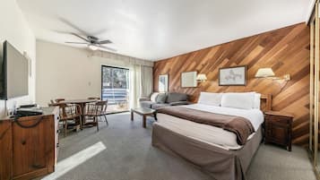 A hotel room with a bed, a desk with a telephone, a chair, a sofa, a ceiling fan, and a window with curtains.