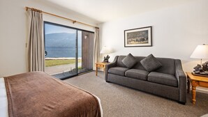 Une chambre d’hôtel comprenant un lit, un canapé, une lampe, une petite table, un tableau au mur et une porte-fenêtre coulissante donnant sur un balcon avec vue sur l’extérieur.