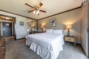 Habitación de hotel con una cama grande, dos mesitas de noche con lámparas, un ventilador de techo y una puerta que da a otra habitación.