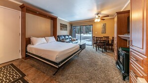 Een hotelkamer met een bed, een zithoek met een tafel en stoelen, een open haard en een groot raam met uitzicht op bomen.