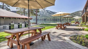 Un área de picnic con mesas y bancos de madera, asadores al aire libre y sombrillas.