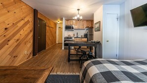 Una habitación pequeña con cama, cocina compacta y pared de madera.