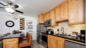 A modern kitchen with wooden cabinets, stainless steel appliances, a black countertop, and a ceiling fan. - 125 Bldg B Condo (Truckee)