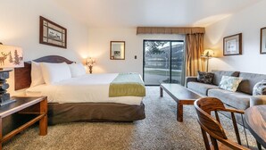 A hotel room with a bed, a sofa, a desk, and a chair. There is a window with a view of a lake and trees. - 144 Bldg C 1 Bedroom Condo (Truckee)