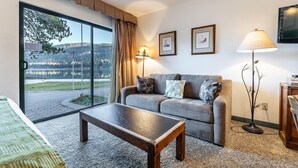 A modern living room with a sofa, a coffee table, and a view of a lake through large windows. - 144 Bldg C 1 Bedroom Condo (Truckee)