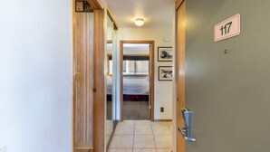 A hallway with a wooden door labeled 117, leading to a room with a bed and a window. - 117 Bldg B 1 Bedroom Condo (Truckee)