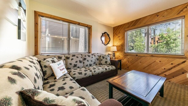 A cozy living room with a sectional sofa, a wooden coffee table, and large windows with blinds. - 117 Bldg B 1 Bedroom Condo (Truckee)