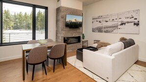 Ein modernes Wohnzimmer mit Kamin, einem Essbereich mit großem Fenster und einem weißen Sofa.