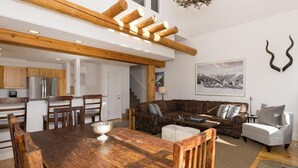 Een ruime woonkamer met een houten eettafel, een bruine leren bank en een grijze fauteuil.