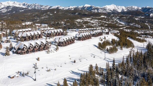 Een besneeuwde ski-resort met rij bungalows, skipistes en een berg op de achtergrond.