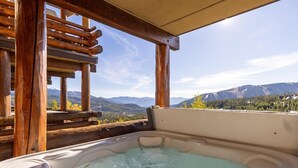 Een hottub met uitzicht op bergen, een houten terras en een pergola.