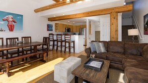 Een ruime woonkamer met een houten eettafel, een bruine bank en een keuken op de achtergrond.