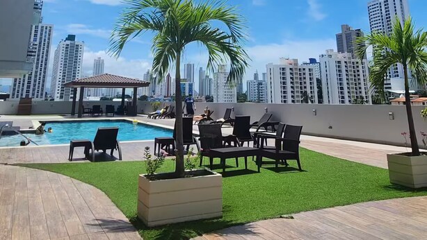Ein Poolbereich auf dem Dach mit einer Holzterrasse, Liegestühlen und einer kleinen Palme.