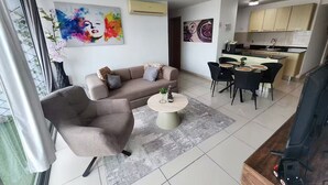 Ein modernes Wohnzimmer mit einer Couch, einem Sessel und einem Couchtisch, ein Essbereich mit Stühlen und Tisch sowie eine Küche mit Schränken und Spüle.