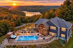 Una casa grande con piscina, jacuzzi y terraza con vista a un lago rodeado de árboles.