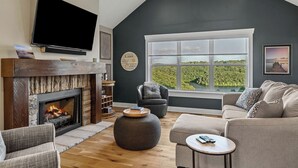 Un salon doté d’une cheminée, d’une grande fenêtre offrant une belle vue, d’un téléviseur à écran plat et d’un ventilateur de plafond.