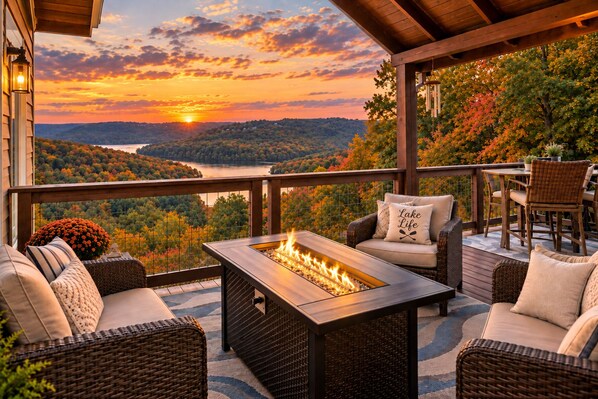 Una terraza con mobiliario exterior, una chimenea y una vista panorámica de un lago y un bosque al atardecer.