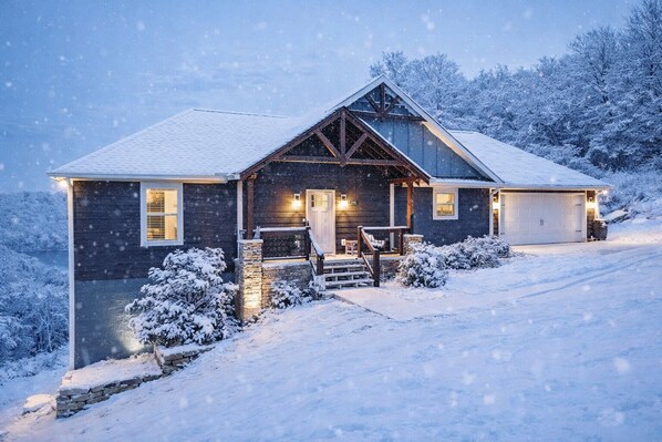 A wooden house with a stone foundation, a front porch, and a garage.